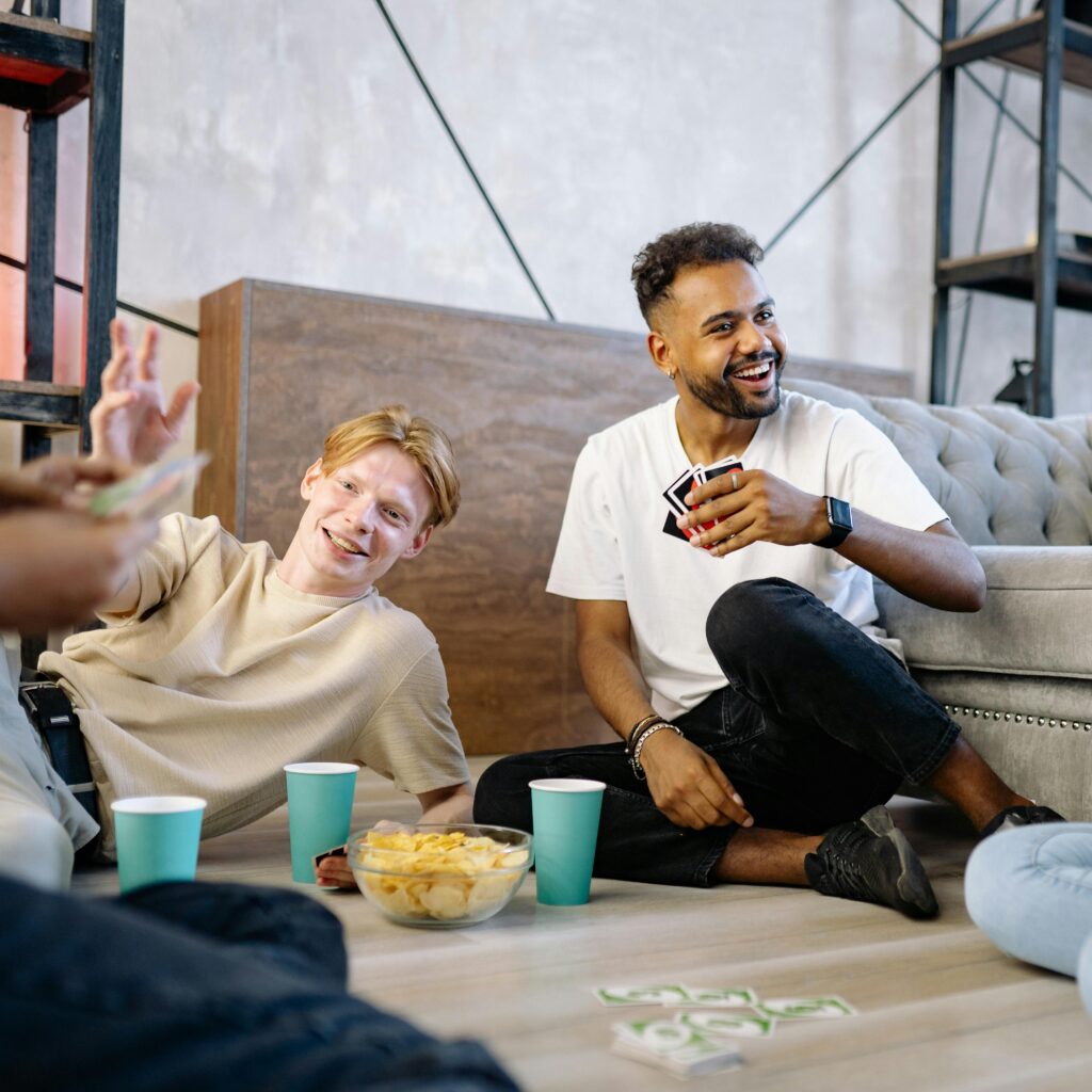 Two friends having fun playing a card game in a cozy indoor setting with snacks.