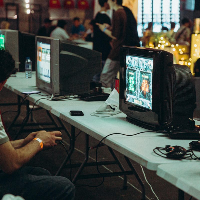 Adults enjoying a retro gaming event with CRT televisions and consoles, creating a nostalgic atmosphere indoors.