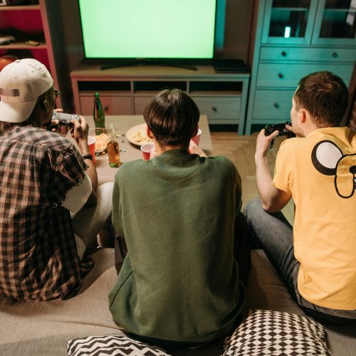 Three young men enjoying a home gaming session together, playing video games in a cozy indoors setting.